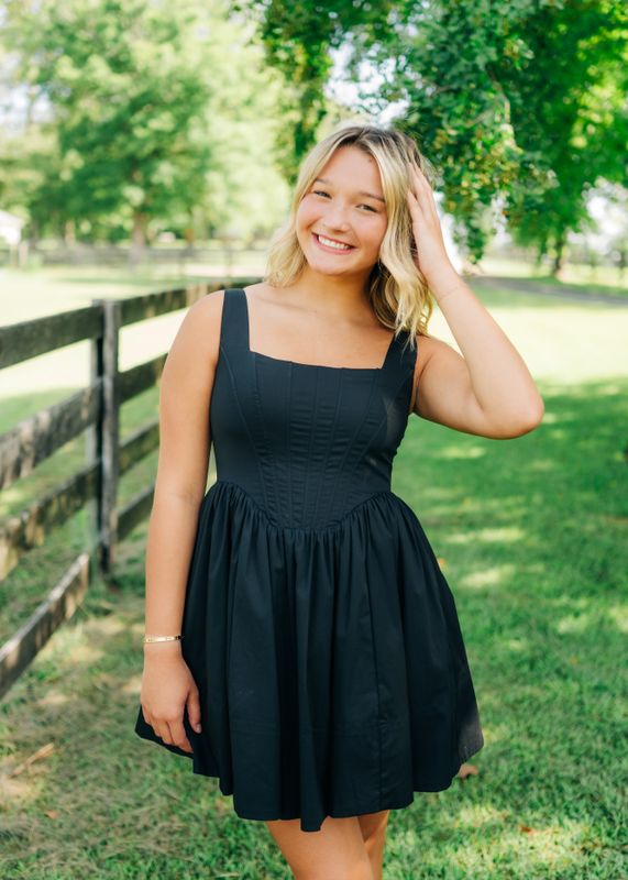 Close-up of black corset bodice dress with structured bodice and pleated skirt, model smiling outdoors.