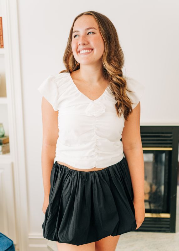Model smiling in a Black Bubble Mini Skirt with a voluminous hem, styled with a white top for a chic day-to-night look.