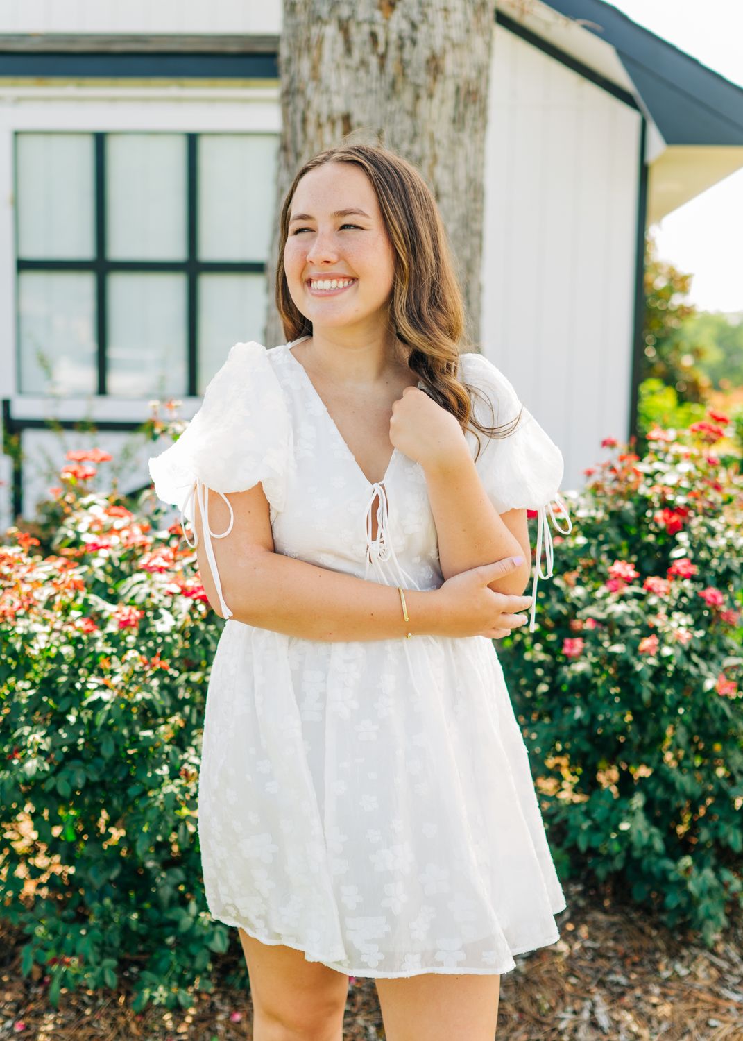Young woman smiling in a white floral puff sleeve mini dress with tie-front detail, styled for summer events.