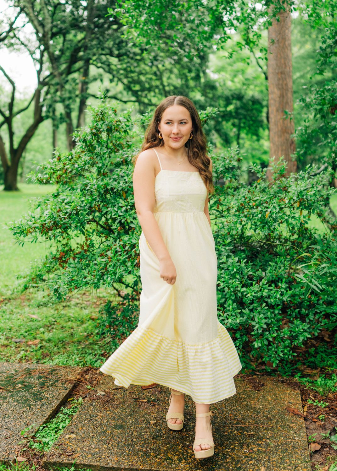 Model wearing lemon yellow maxi dress with embroidered bodice and striped hem, walking outdoors.