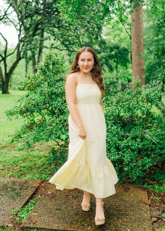 Model wearing lemon yellow maxi dress with embroidered bodice and striped hem, walking outdoors.