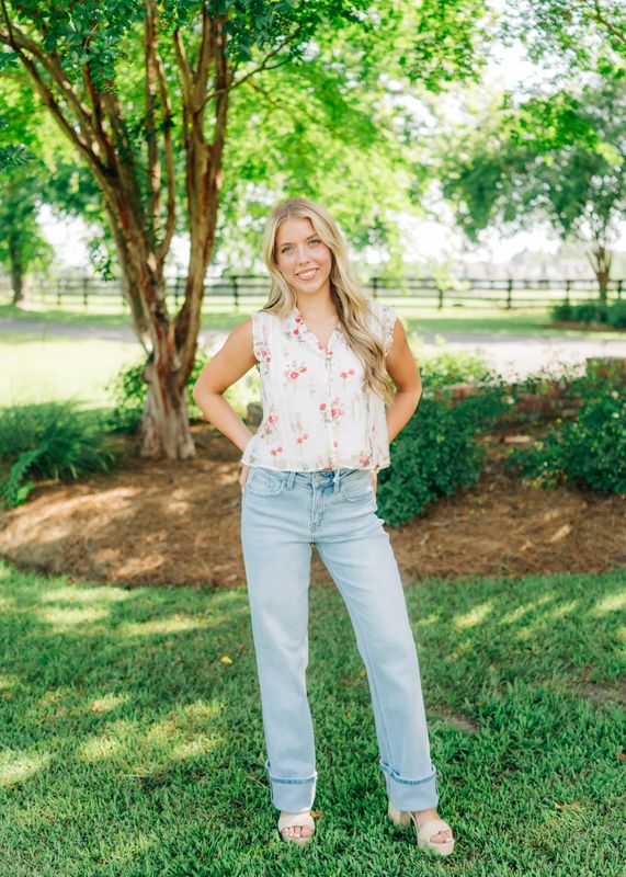 Back view of woman wearing a white sleeveless floral blouse with ruffle trim, paired with light wash jeans.