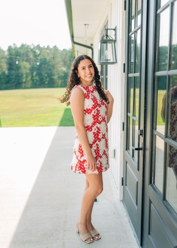 Smiling model in red &amp; white shift dress standing by white barn doors.