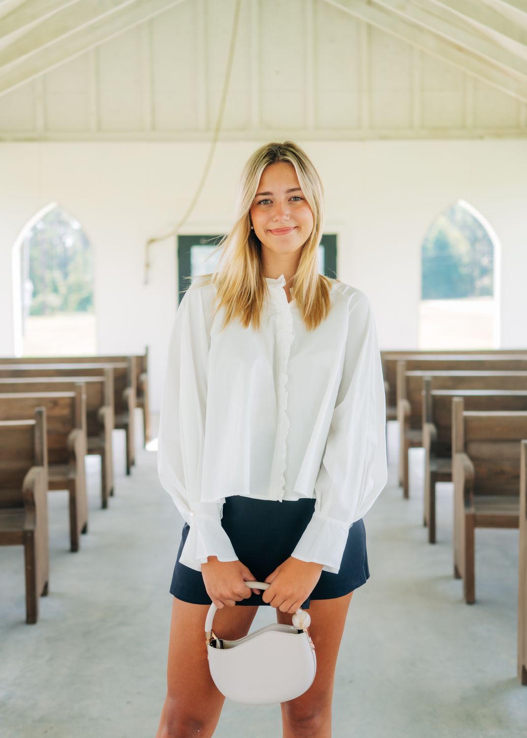 Model smiling in white ruffle blouse with loose sleeves and ruffle-front detail.