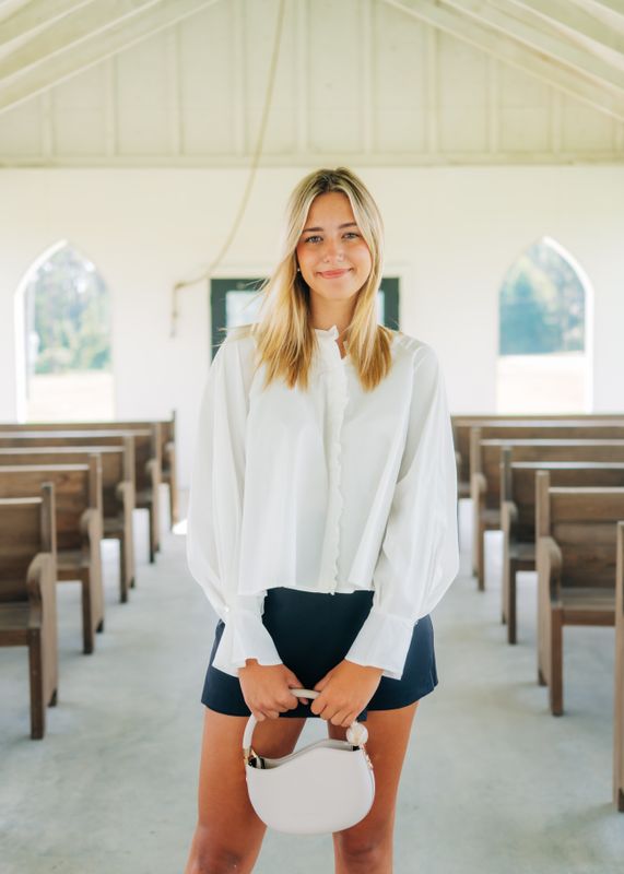 Model smiling in white ruffle blouse with loose sleeves and ruffle-front detail.
