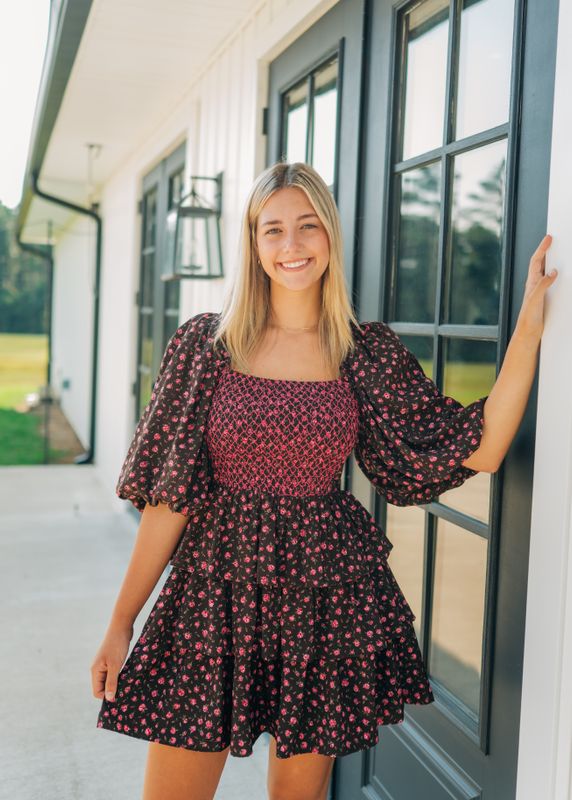 Model wearing dark brown floral puff sleeve mini dress with smocked bodice, smiling outdoors
