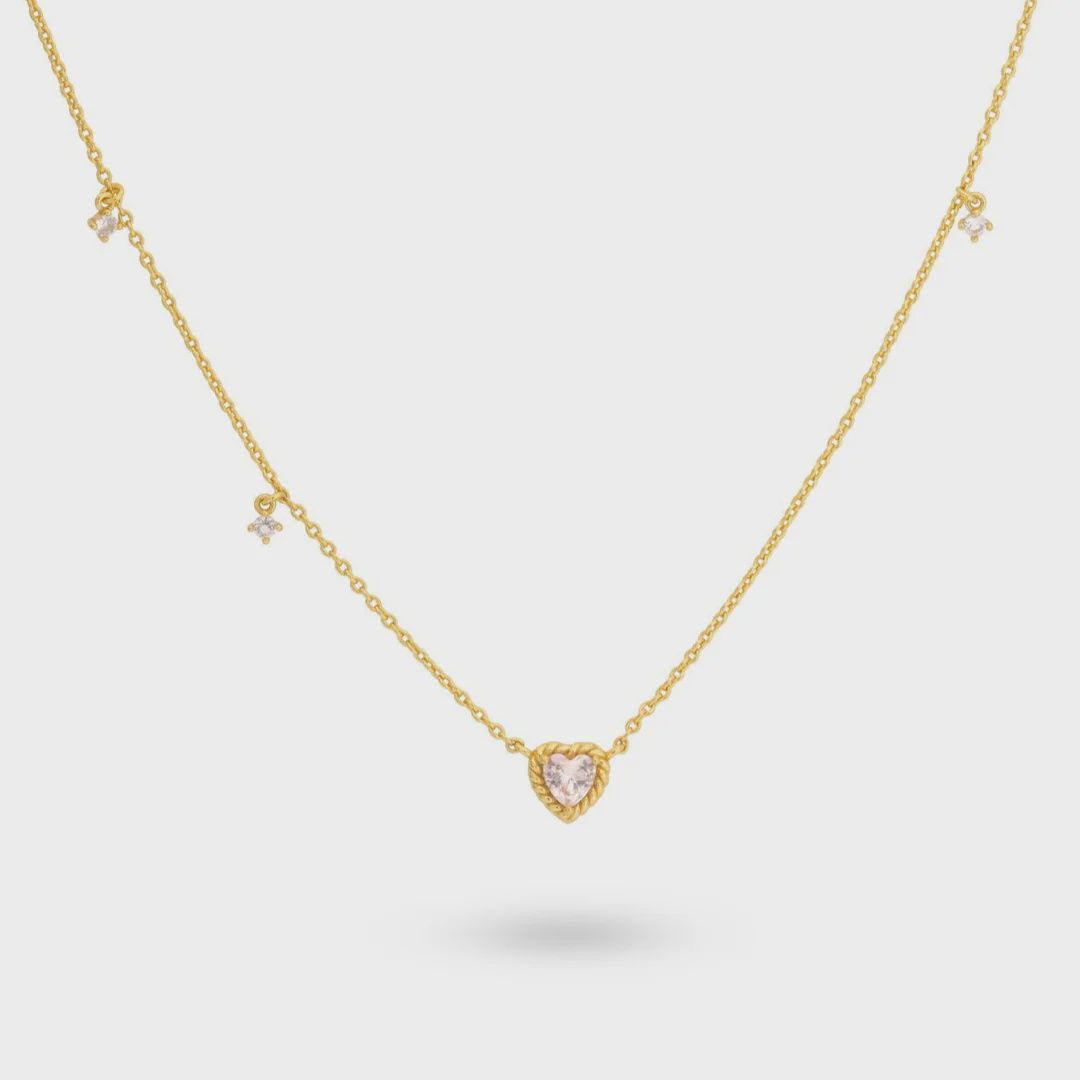 Een vergulde zilveren ketting met een roze hartvormige steenhanger, aangevuld met drie asymmetrisch geplaatste stenen langs de ketting