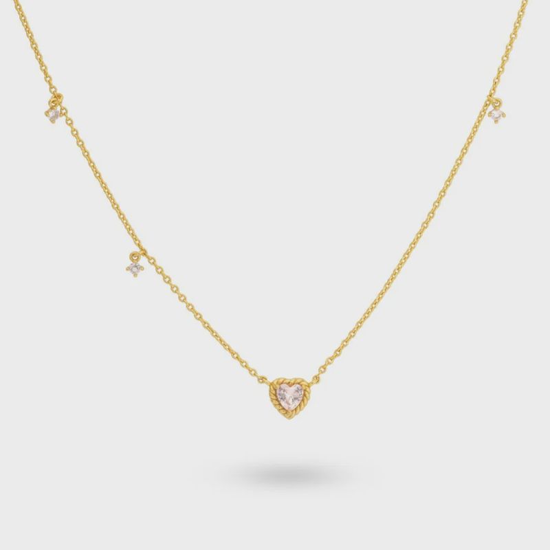 Een vergulde zilveren ketting met een roze hartvormige steenhanger, aangevuld met drie asymmetrisch geplaatste stenen langs de ketting