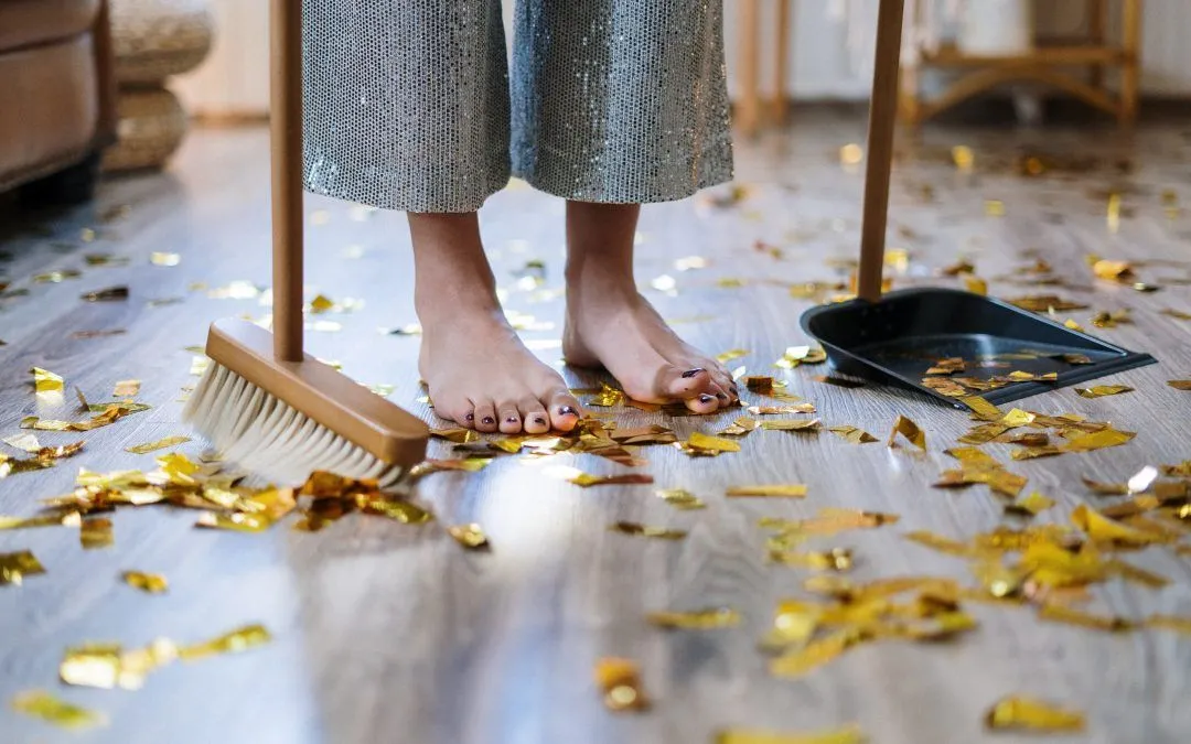 A person is standing on a messy floor with a broom and dustpan.