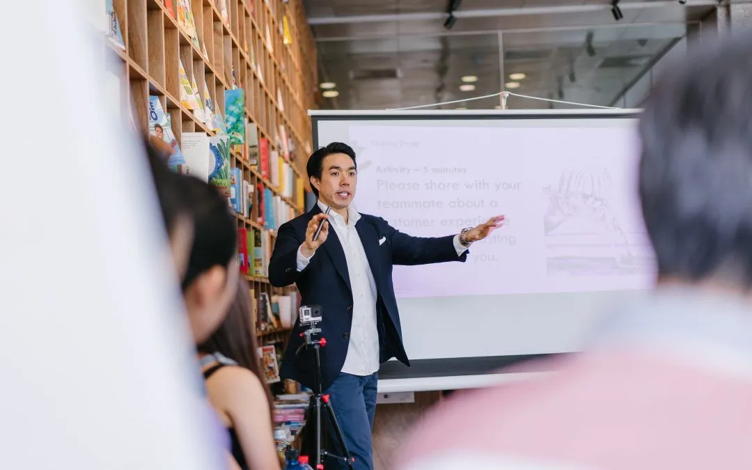 A man is giving a presentation to a group of people in front of a projector screen.