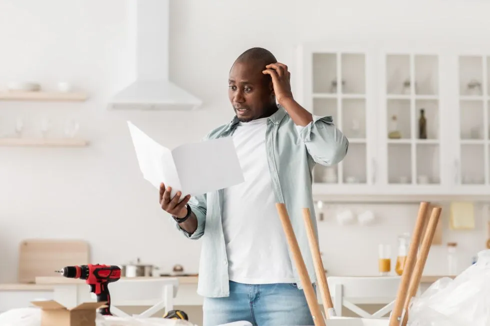 A man is standing in a kitchen looking at a piece of paper.