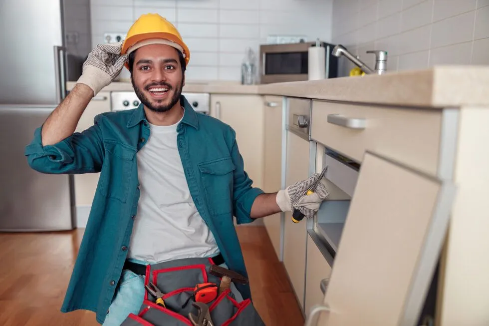 A man is wearing a hard hat and holding a screwdriver in a kitchen.