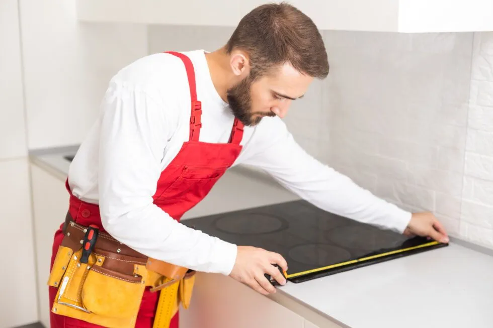 A man is measuring a stove top with a tape measure.