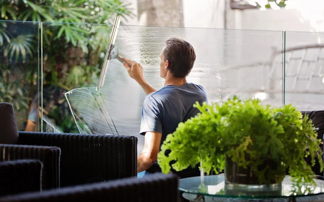 A man is cleaning a window with a squeegee in a living room.