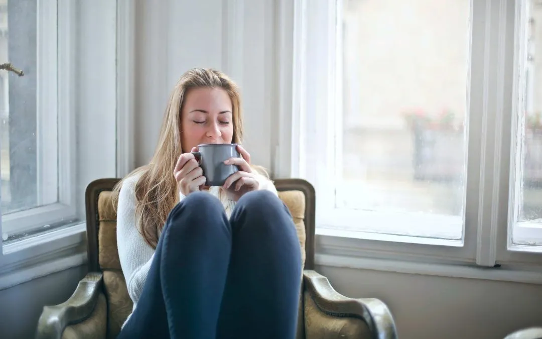 A woman is sitting in a chair drinking a cup of coffee.