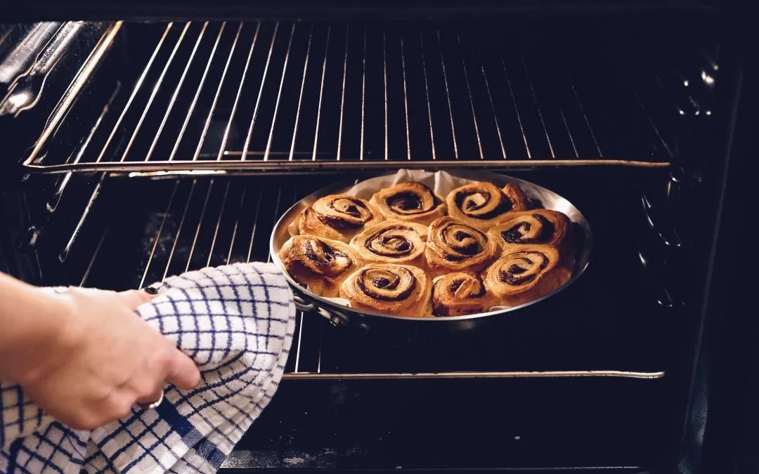 A person is taking a pan of cinnamon rolls out of the oven.