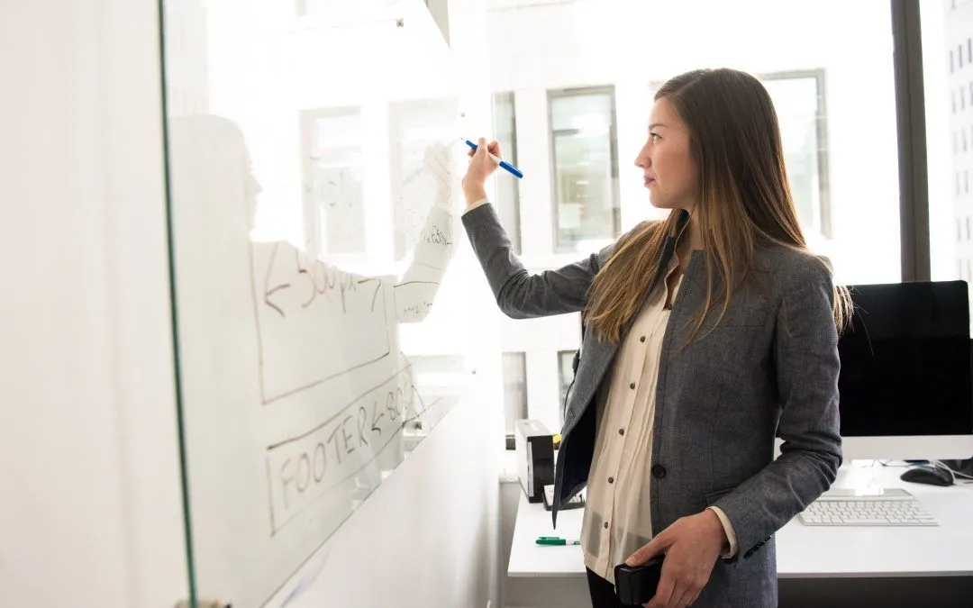 A woman is writing on a whiteboard in an office.