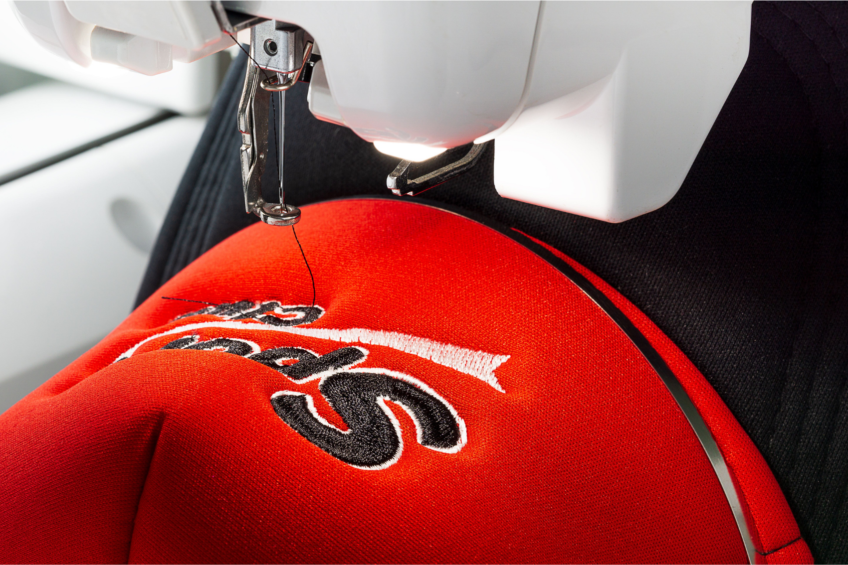 The image shows unassembled baseball cap fabric panels laid out flat on a white background, with embroidery across the seams and edges, in an industrial factory setting.