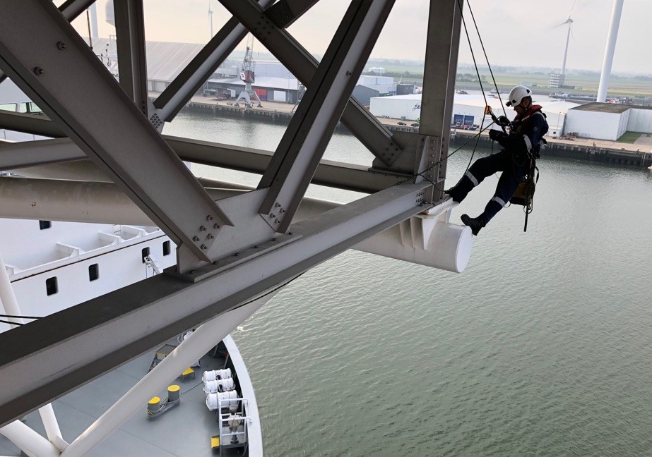 Rope access technician performing structural inspection on steel framework above water.