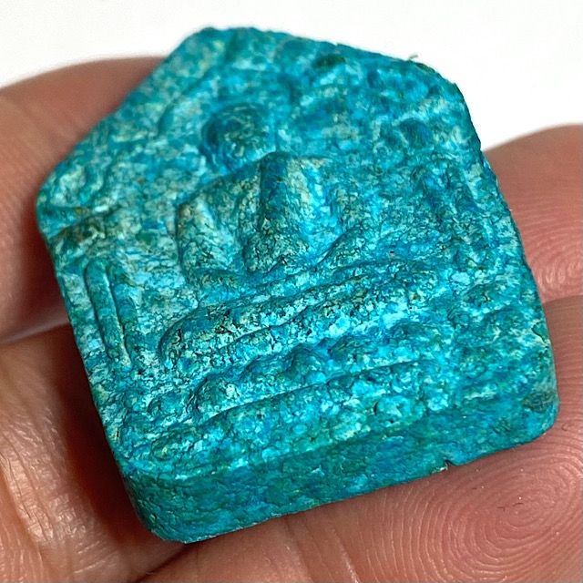 Close up of the front face of the amulet seen from an angle from the bottom edge held in the hand