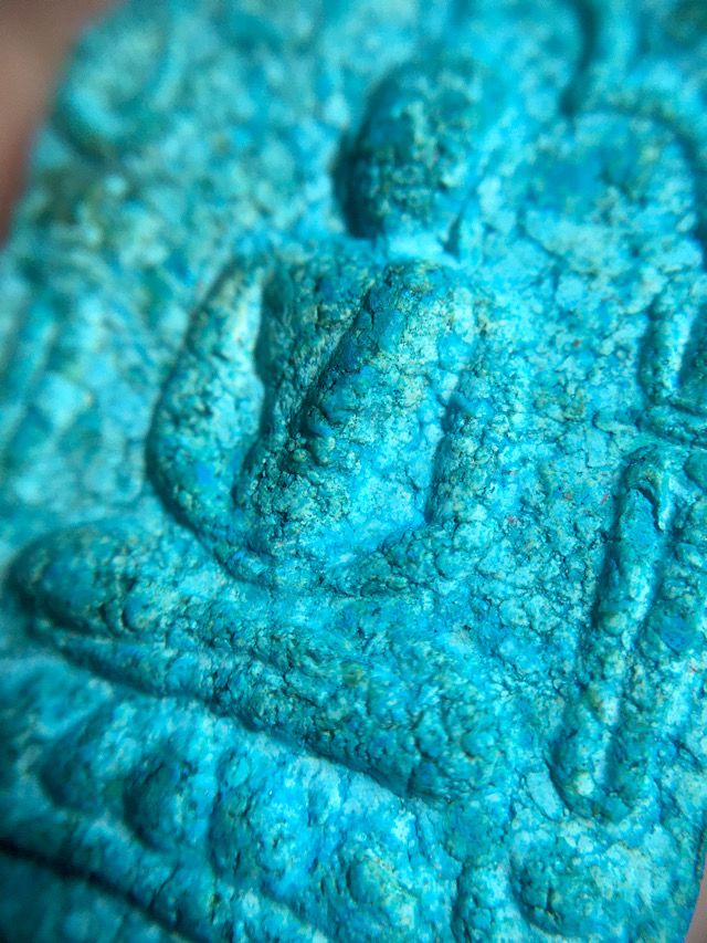 Close up of the image of the Buddha on the front face of the amulet showing the highly detailed relief and the visibly authentic sacred powder clay