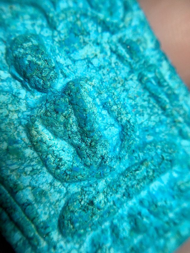 Close up image of the front face of the amulet from the side showing the chest arms and face of the Buddha in the central section