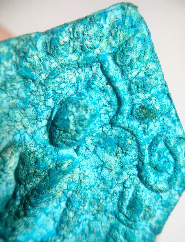 Close up of the front face of the amulet focusing on the top section and the arch and the face and shoulders of the Buddha