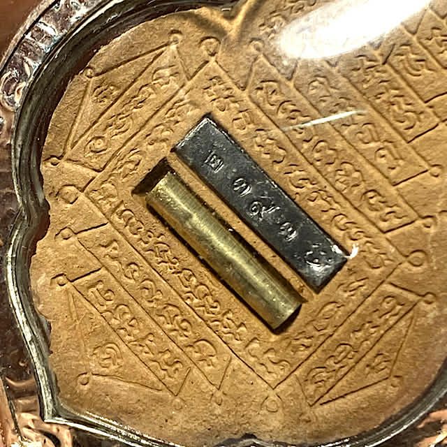 close up of The rear face of the amulet Pra Rahu Luang Pu Bun Ma with Takrut spell and code stamp embedded into the Muan Sarn and the Yantra on the rear face
